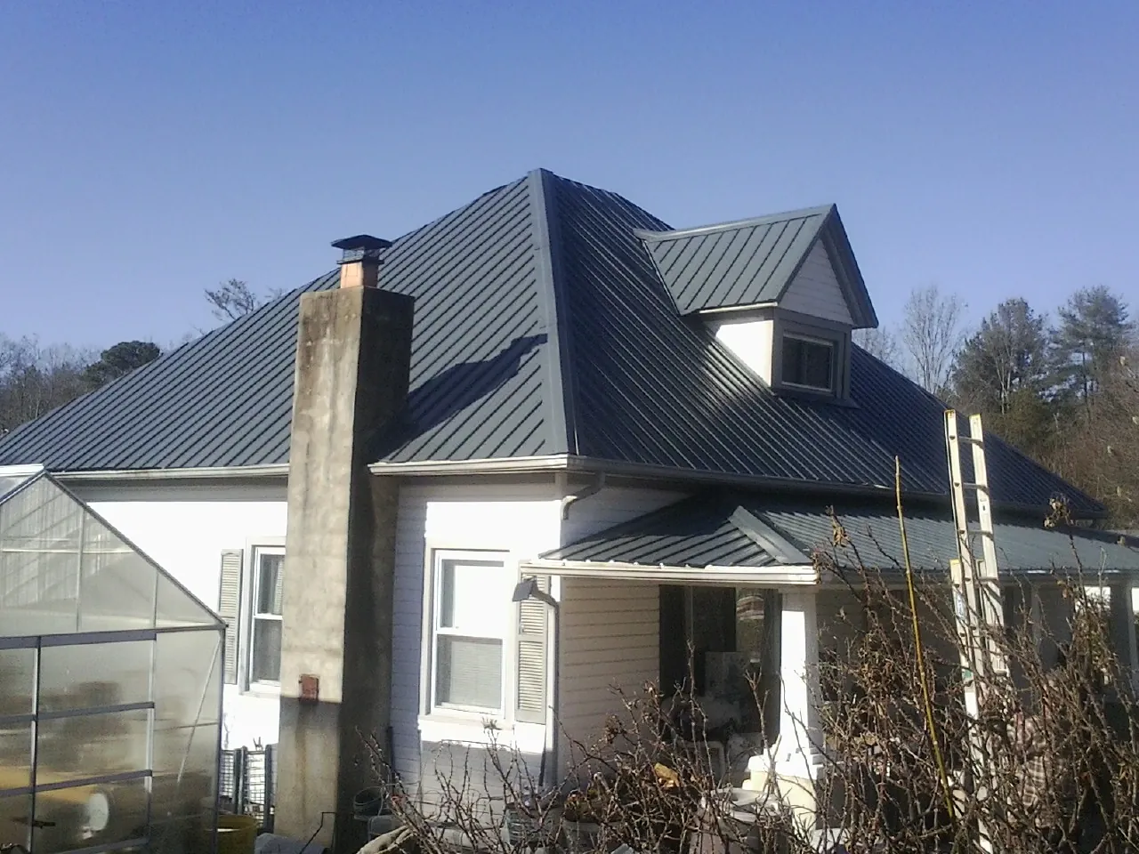 Dark blue standing seam metal roof on a white farmhouse with dormer — Slate & Tile Roof Repair by Roofing Brothers in Sand Lake
