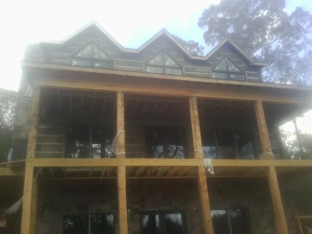 Dormers and porch framing on a large log home under construction — Roof Coating work by our crew in Sand Lake