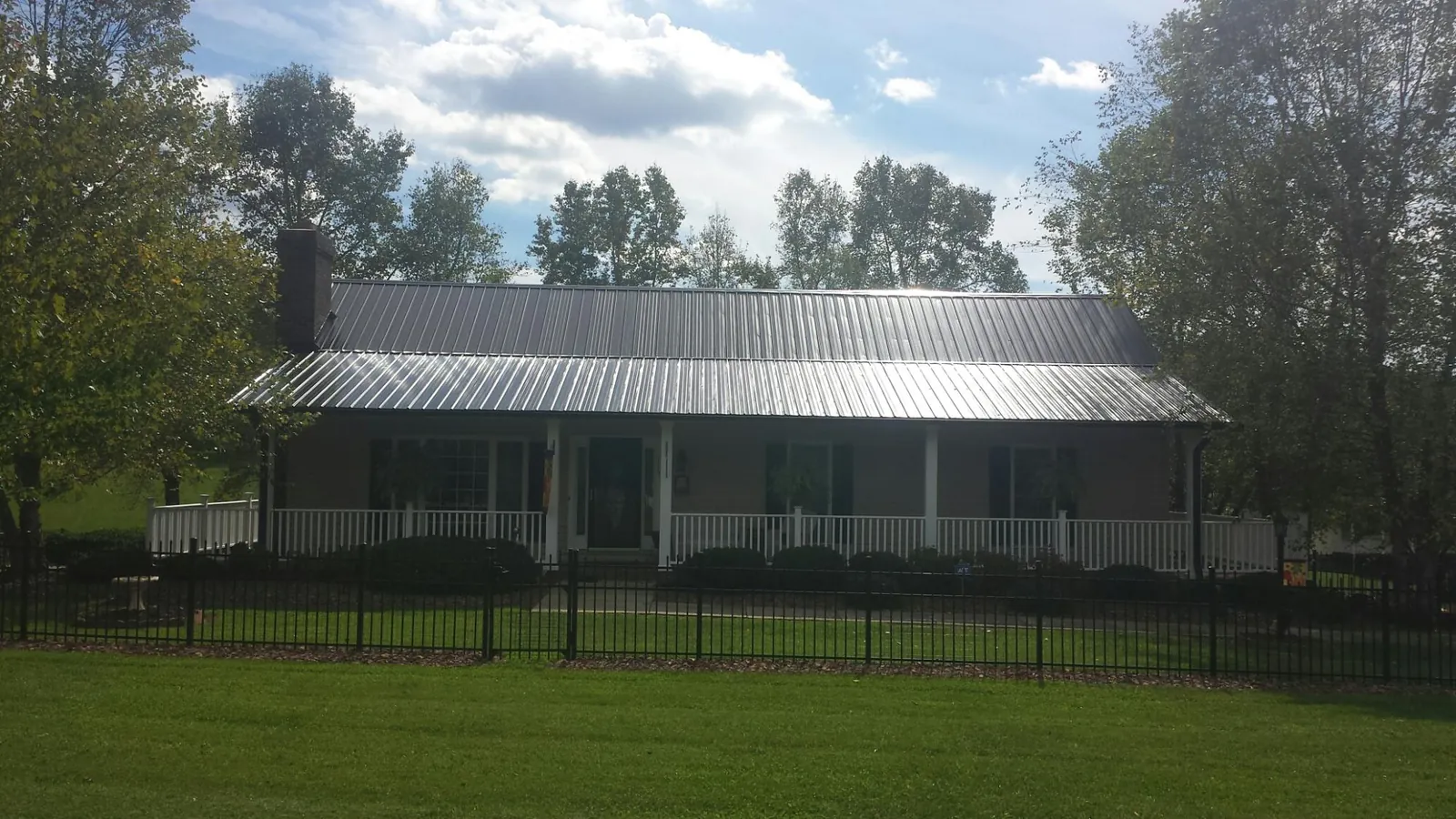 Gray metal roof on a brick ranch with a full width front porch — Gutter Guard Installation work by our crew in Sand Lake
