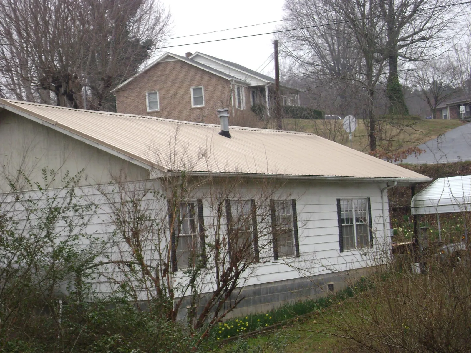 Tan metal roof on a white sided house set into a hillside — Commercial Roofing by Roofing Brothers in Sand Lake